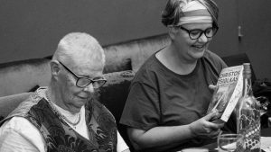Two senior women reading and enjoying books together in a cozy indoor setting.
